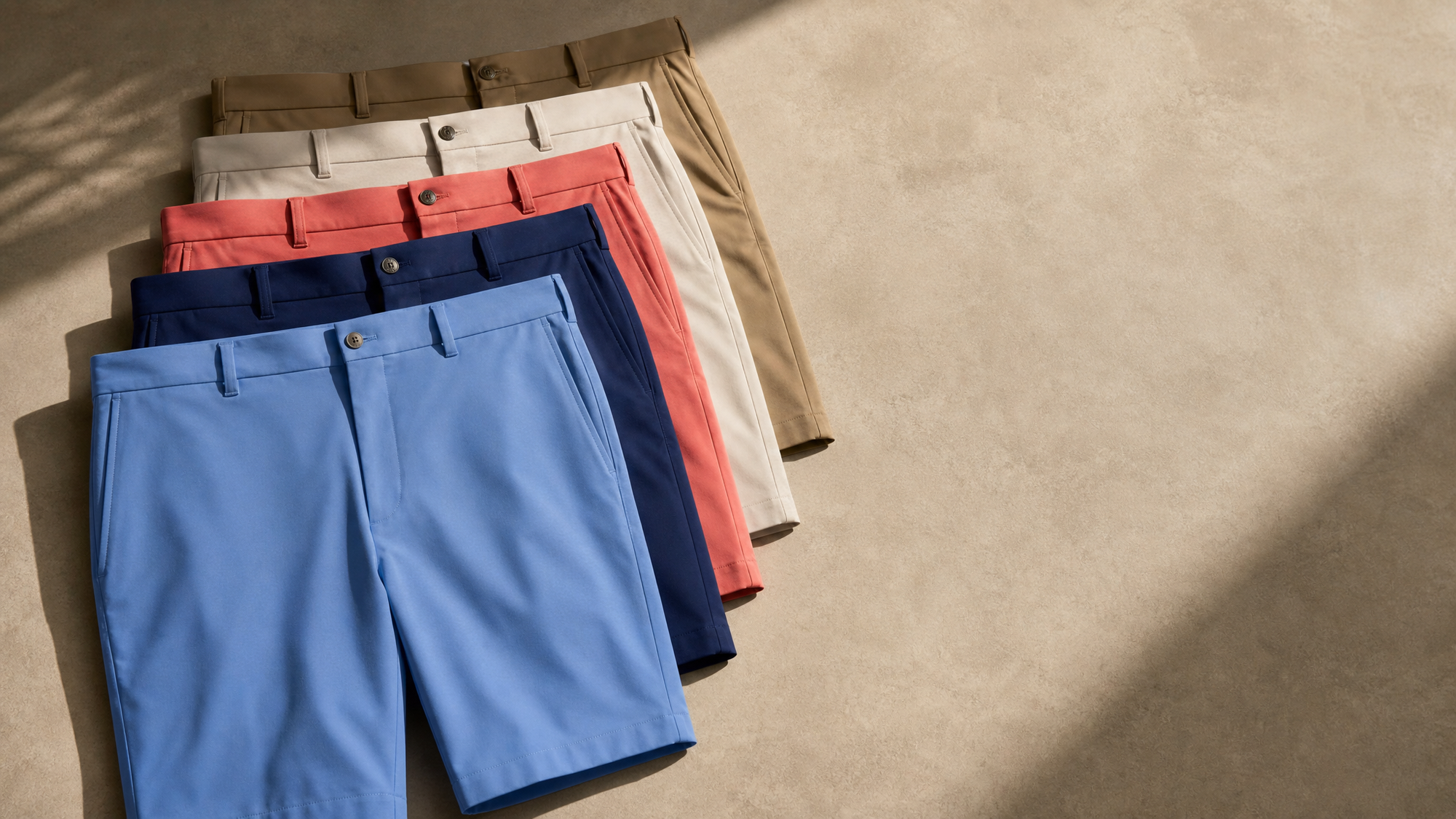Layered men's golf shorts in light blue, navy, coral, khaki, and stone, highlighting classic summer style and performance comfort.